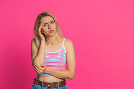 Displeased exhausted Caucasian young woman rubbing temples to cure headache problem, suffering from tension, migraine, stress. Blonde girl grimacing in pain, high blood pressure on pink background