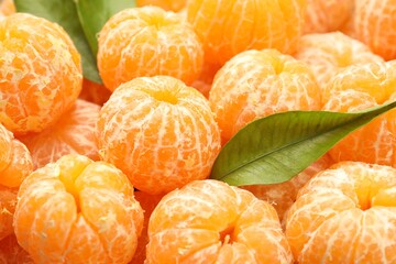 Many ripe peeled tangerines and green leaves, closeup