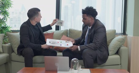 Professional business meeting between two colleagues discussing architectural plans and real estate development. Analyzing blueprints and project layouts with a cityscape in the background.
