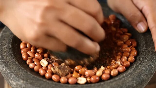 Hands Making Gado Gado Sauce Grinding Peanuts and Palm Sugar in Stone Mortar for Indonesian Salad Dressing Recipe Close