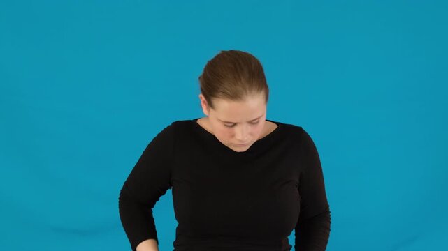 Woman stands in studio and checks pockets for missing object. Female looks for lost thing in spacious studio on blue background