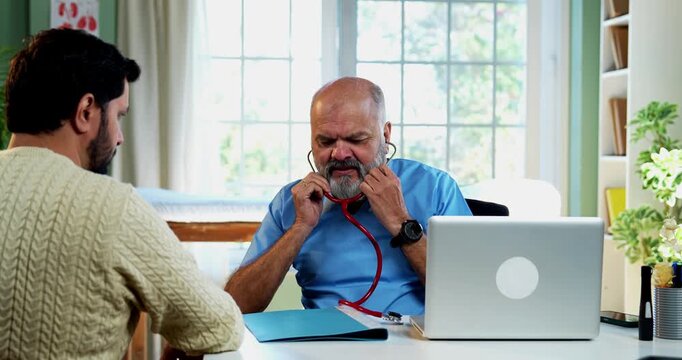 Indian male doctor treating patient during routine health checkup as experienced physician examines young man with stethoscope in modern Indian clinic OPD healthcare consultation visit