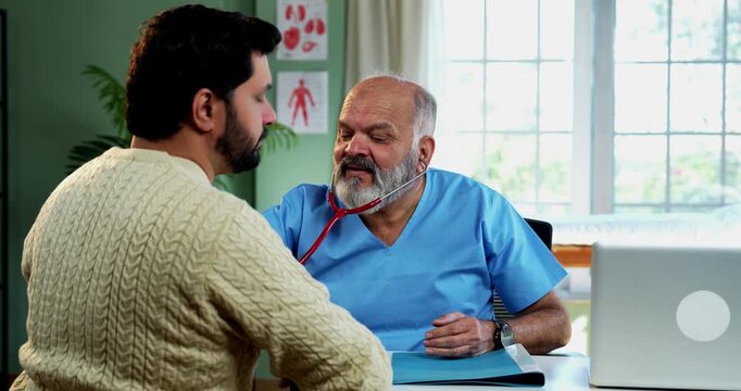 Indian male doctor treating patient during routine health checkup as experienced physician examines young man with stethoscope in modern Indian clinic OPD healthcare consultation visit