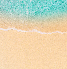 A close-up, aerial view of clear, turquoise ocean water gently washing onto a sandy beach. The...