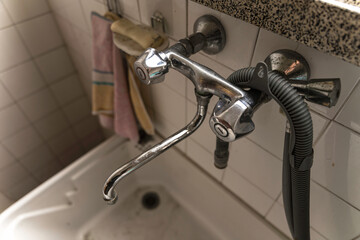Old chrome faucet with shower hose above sink