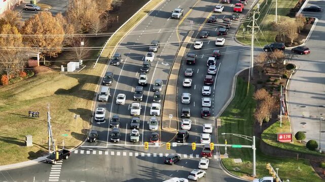 Aerial view of heavy traffic on multi-lane road in United States during late autumn or winter, with cars queued at an intersection under clear sunlight and bare trees. Pedestal up wide shot,
