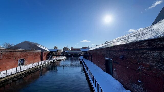 Visitors walking beside a snowy waterfront warehouse at Hakodate Bay
