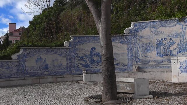 Slow pan across a historic azulejo tile fountain and small coastal park in Paco de Arcos, with blue and white ceramic artwork and calcada portuguesa pavement on a sunny day.