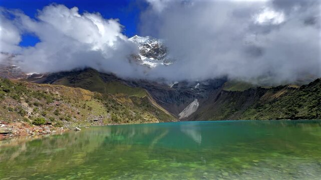Peruvian Andes Mount Humantay Laguna Lake Peru Per&uacute; Salkantay high altitude prominent snow capped glacier mountain peaks morning blue sky clouds fog sunny Anta province dry rainy season pan left