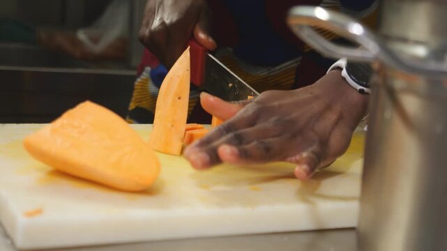 A detailed look at a african chef's knife skills while preparing nutrient-rich orange-Fleshed yams Ipomoea batatas for a traditional soup base.
