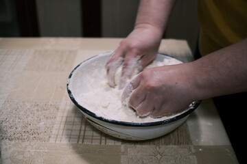 Hands mixing dough in a bowl on a kitchen table, homemade baking process with flour and grated...