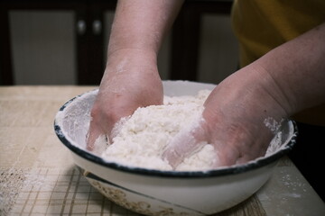 Hands mixing dough in a bowl on a kitchen table, homemade baking process with flour and grated...