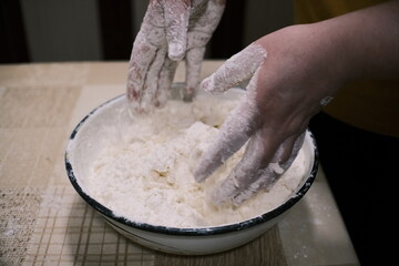 Hands mixing dough in a bowl on a kitchen table, homemade baking process with flour and grated ingredients, close-up food preparation scene showing rustic home cooking and traditional cuisine.