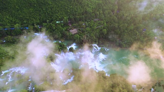 High-angle drone shot of Ban Gioc Waterfalls in Cao Bang. Majestic multi-tiered cascades surrounded by lush green mountains and mist, located on the border between Vietnam and China.
