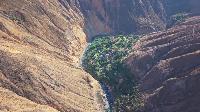 A low bird&rsquo;s-eye drone flies over Colca Canyon&rsquo;s lush oasis at sunrise. Golden light bathes the vibrant vegetation, while the Rio Colca winds gracefully, highlighting the canyon&rsquo;s natural paradise.