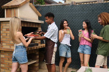 Group of young people having fun grilling sausages and drinking lemonade in the backyard