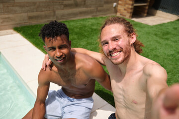 Two male friends are enjoying their summer vacation, taking a selfie by the pool