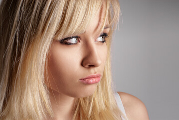 Fototapeta premium Blonde woman gazing thoughtfully to the side, exuding a pensive and reflective mood, captured against a neutral gray backdrop.
