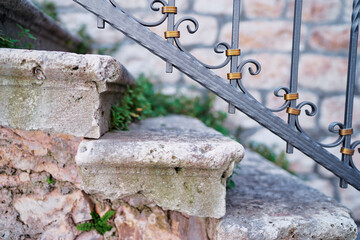 Close up of weathered stone steps with decorative wrought iron railing, rustic Mediterranean architectural detail.