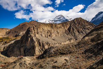 Obraz premium Eroded cliffs and ancient cave formations along the trekking route from Muktinath to Kagbeni in the Kali Gandaki Valley, Nepal. The arid, rugged landscape of the Mustang region contrasts with snow-cov