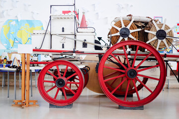 Vintage fire engine with large red wheels and hose reels on display indoors.