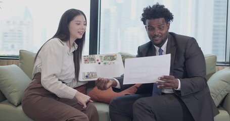 Professional business meeting between two colleagues discussing architectural plans and real estate development. Analyzing blueprints and project layouts with a cityscape in the background.
