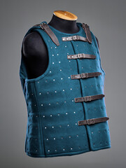 Blue padded gambeson featuring silver metal studs and adjustable leather straps, commonly used in costumes and armor reenactments or medieval wear for protection and aesthetics during period roleplay.