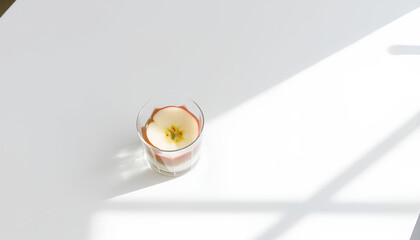 Minimalist white table setting with a clear beverage and glass apple slices inside, with shadows from window light