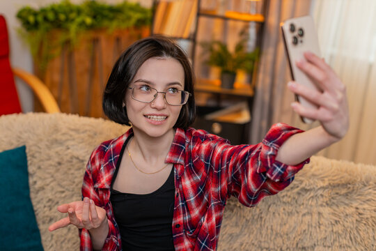 Blogger woman records herself on smartphone at home, smiling and talking with viewers through video vlog. Girl gestures cheerfully, creating lively online diary and sharing joyful energy with audience