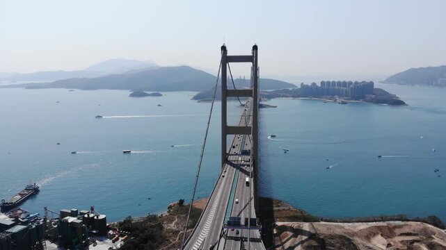 Quick lengthwise shot of Tsing Ma bridge from Tsing Yi island side. Two legged pylon, light traffic on Lantau link highway, mountainous islands seen at distance, small boats and ships move at water