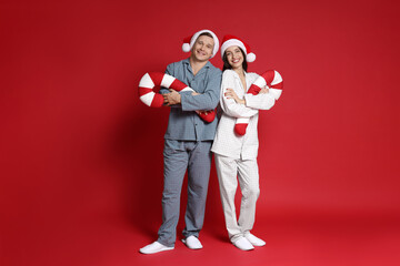 Happy couple in Santa hats and decorative candy canes on red background. Christmas atmosphere