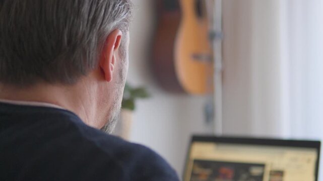 A middle-aged Caucasian man works on a laptop in an apartment - focused closeup over his shoulder