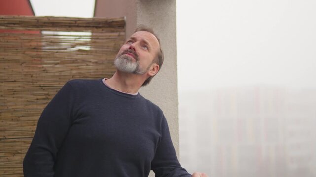 A handsome middle-aged man thinks and looks around on a balcony