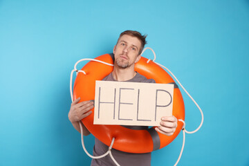 Unhappy man with lifebuoy and cardboard sign with word Help on light blue background