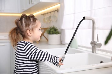 Child safety at home. Little girl pulling down faucet hose at sink in kitchen