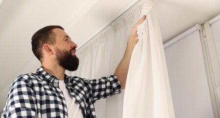 Man hanging up window curtains at home, low angle view. Space for text