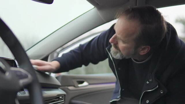 A handsome middle-aged man cleans the dashboard of his car with a cloth - view from the driver's seat