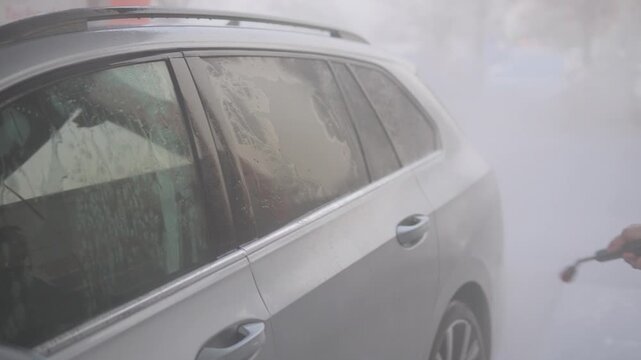 A man power washes the rear door of his car - closeup