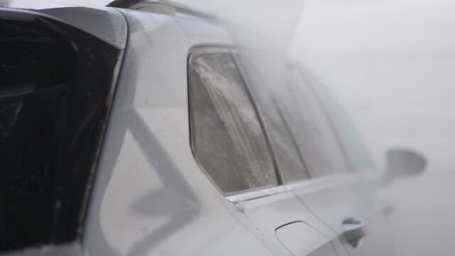 A man power washes the side of his car - closeup from behind a tail light