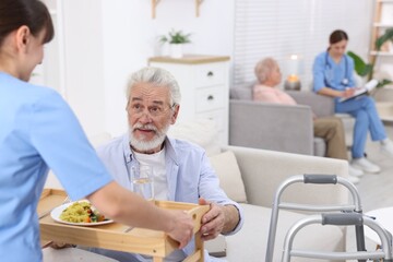 Obraz premium Care worker serving dinner to senior man at retirement home, closeup