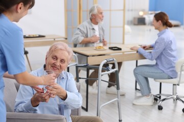 Obraz premium Care worker giving glass of water to senior woman at retirement home, closeup