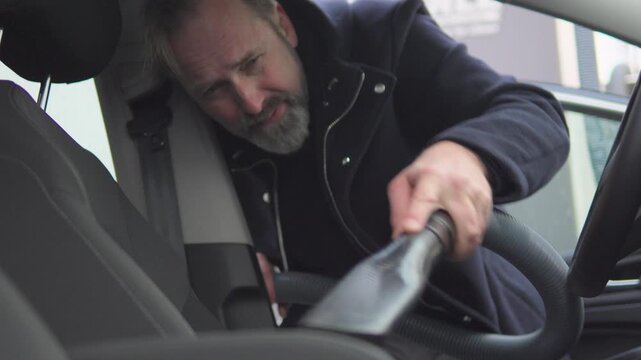 A handsome middle-aged man vacuums the front seats in his car - view from the passenger seat