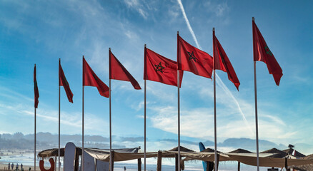 Sunlit Beach Scene With Flags, Red Walkway, And Empty Lounge Chairs At Sunset, Agadir, Morocco © Frankix
