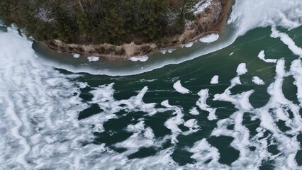 Aerial view shows a river with ice floes.  Water appears dark green.  Forest borders the riverbank.  Snow covers the trees.  The scene depicts a wintry landscape