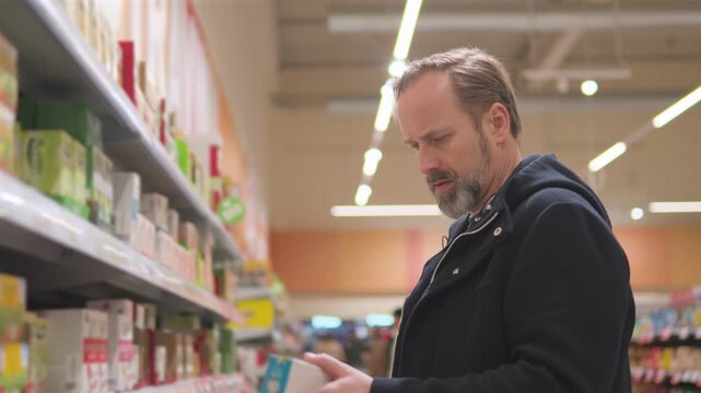 A handsome middle-aged man picks tea from a shelf in a supermarket