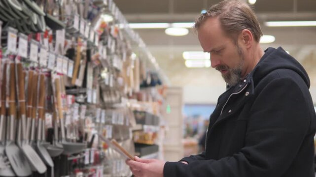 A handsome middle-aged man browses through cooking utensils and picks a metal spatula