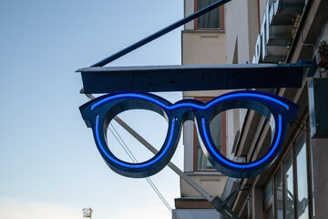 Optician&acute;s neon sign hanging on building wall outdoors