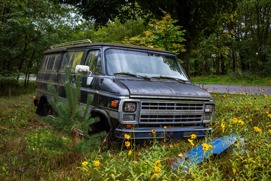 Gray American van abandoned in the woods. The vehicle eaten away by rust and covered in moss.