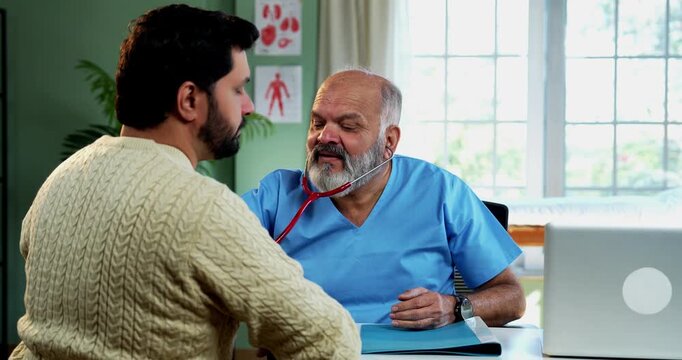 Indian male doctor treating patient during routine health checkup as experienced physician examines young man with stethoscope in modern Indian clinic OPD healthcare consultation visit