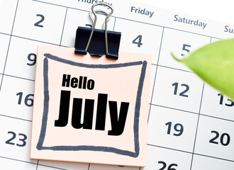 Hello July word on a small piece of paper and a calendar.